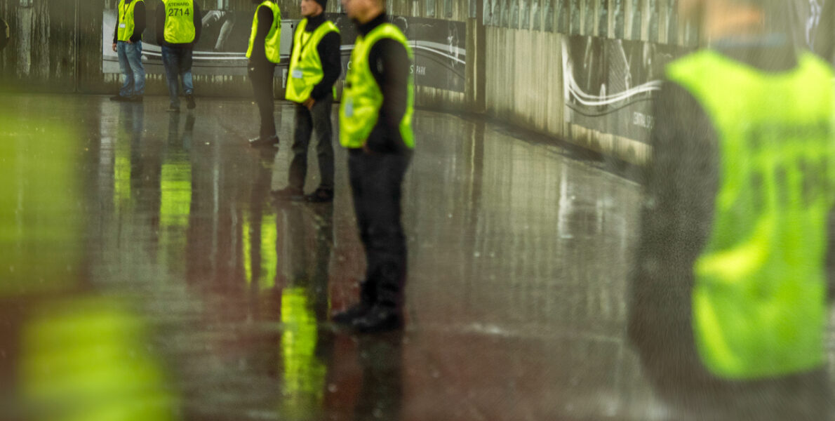 Security employees standing in a line at a stadium on a sporting event at night.